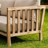 Wooden outdoor Porthallow sofa with beige cushions on a grassy area