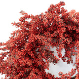 A close-up of a decorative wreath or floral arrangement covered in dense clusters of small red berries with muted brown foliage, shown against a plain white background.