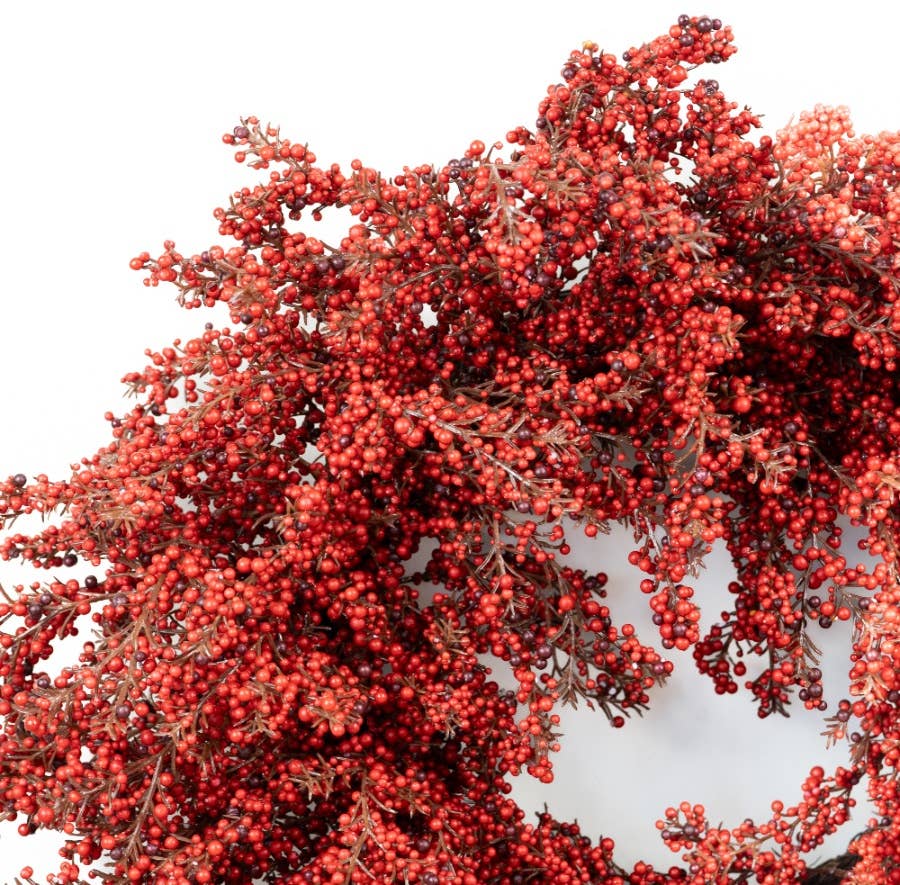 A close-up of a decorative wreath or floral arrangement covered in dense clusters of small red berries with muted brown foliage, shown against a plain white background.
