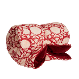 A rolled-up quilted blanket featuring a red and cream floral pattern on the exterior and a plush dark red velvet lining visible on the underside, set against a plain white background.
