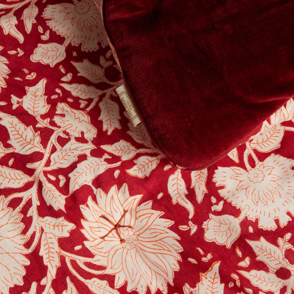 A close-up of a red velvet throw blanket with a cream floral and leaf pattern, partially folded to reveal the plush texture.