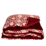 A folded plush throw eaturing a red and cream floral pattern on one side and a solid deep red velvet reverse side, shown against a plain white background.