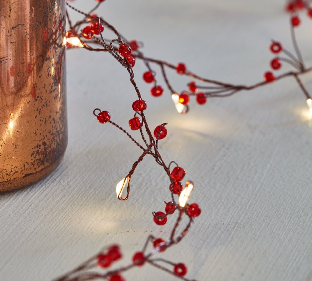 Battery operated white leaf and copper wire string lights with red jewel clusters, designed for Christmas or dinner parties.