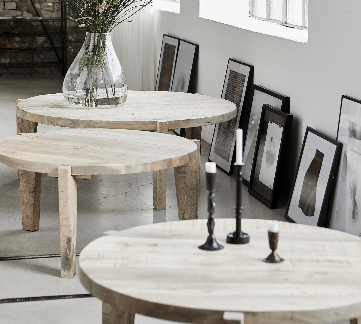 Three round light wood nesting tables in different sizes arranged in a bright, modern room with framed art on the wall.