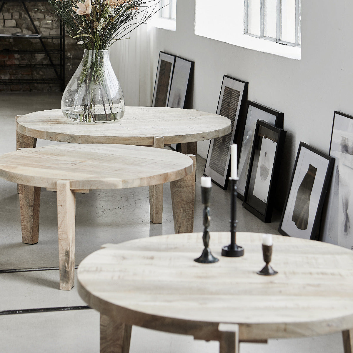 Three round light wood nesting tables in different sizes arranged in a bright, modern room with framed art on the wall.