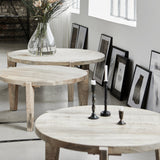 Three round light wood nesting tables in different sizes arranged in a bright, modern room with framed art on the wall.