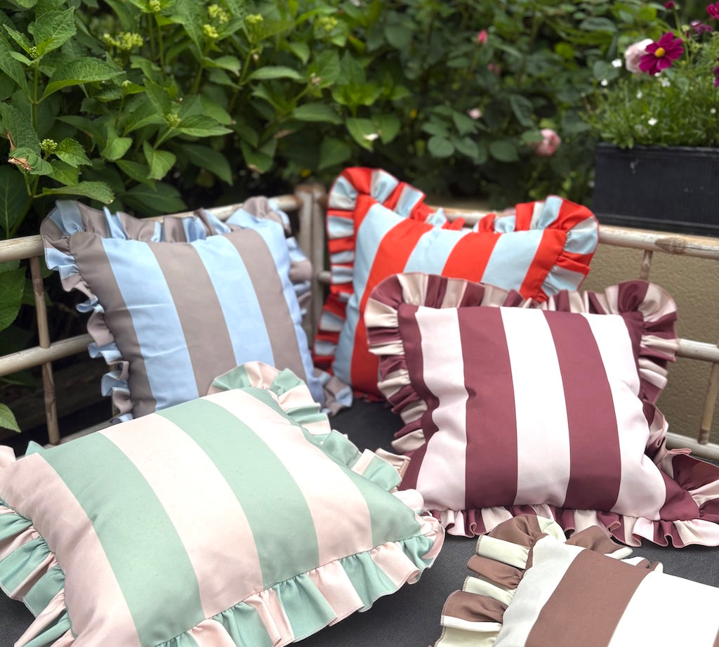 Colorful striped pillows with ruffled edges on a chair outdoors.