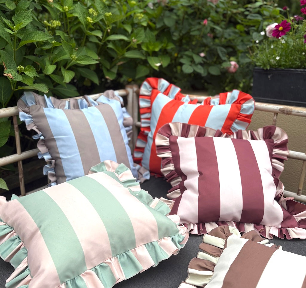 Colorful striped pillows with ruffled edges on a chair outdoors.