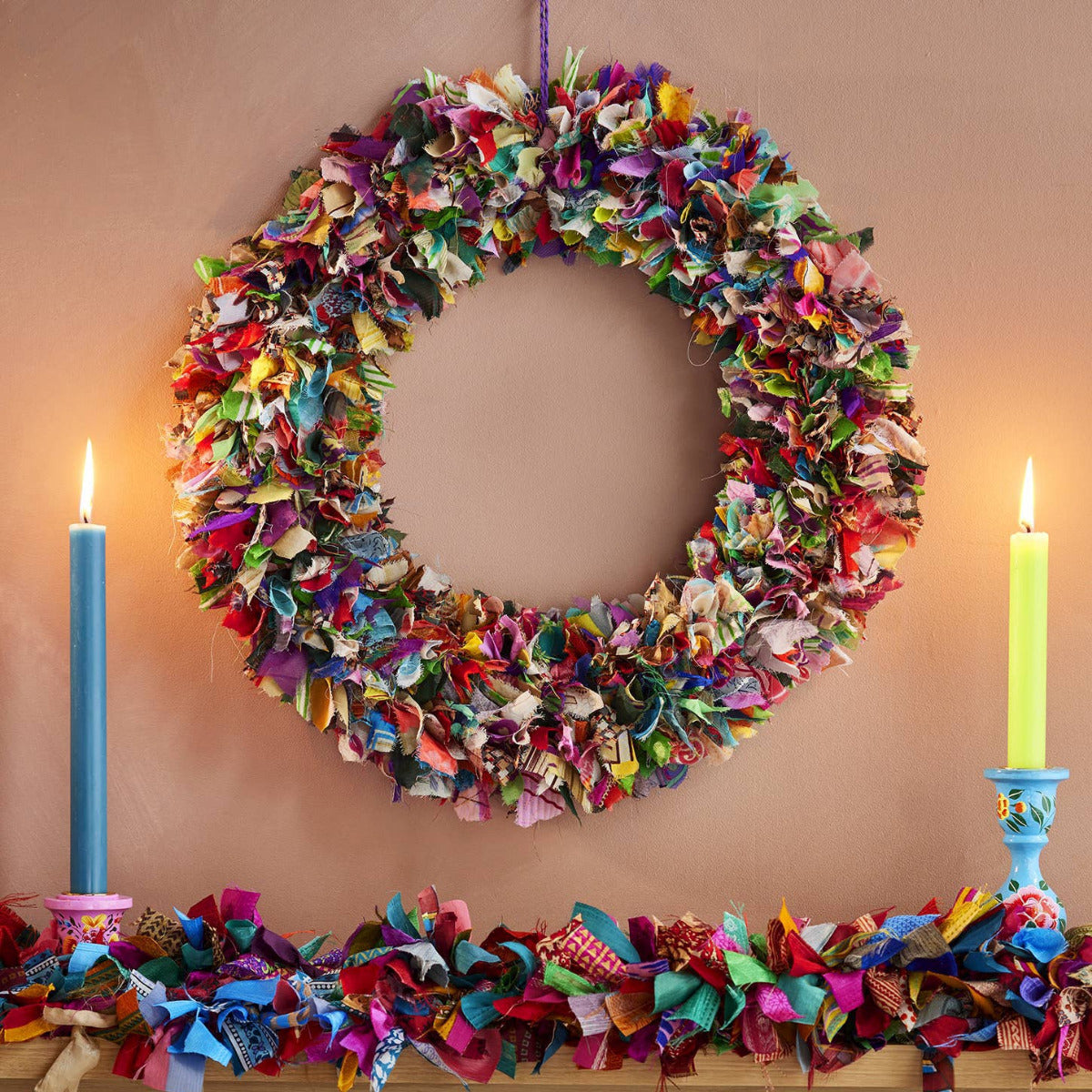 Colorful fabric wreath and garland on a wooden surface with candles.