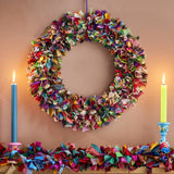 Colorful fabric wreath and garland on a wooden surface with candles.