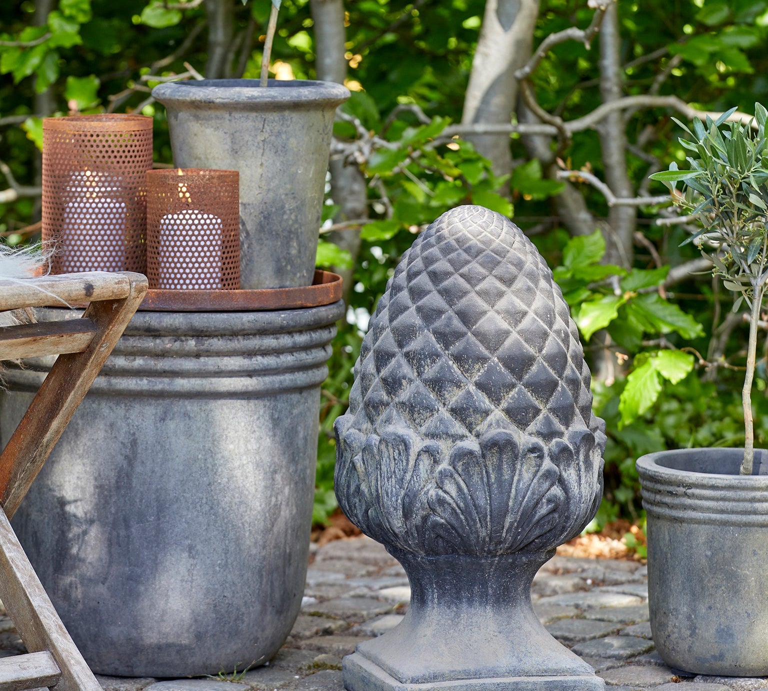 Decorative outdoor setting with potted plants and a stone finial against a natural background.