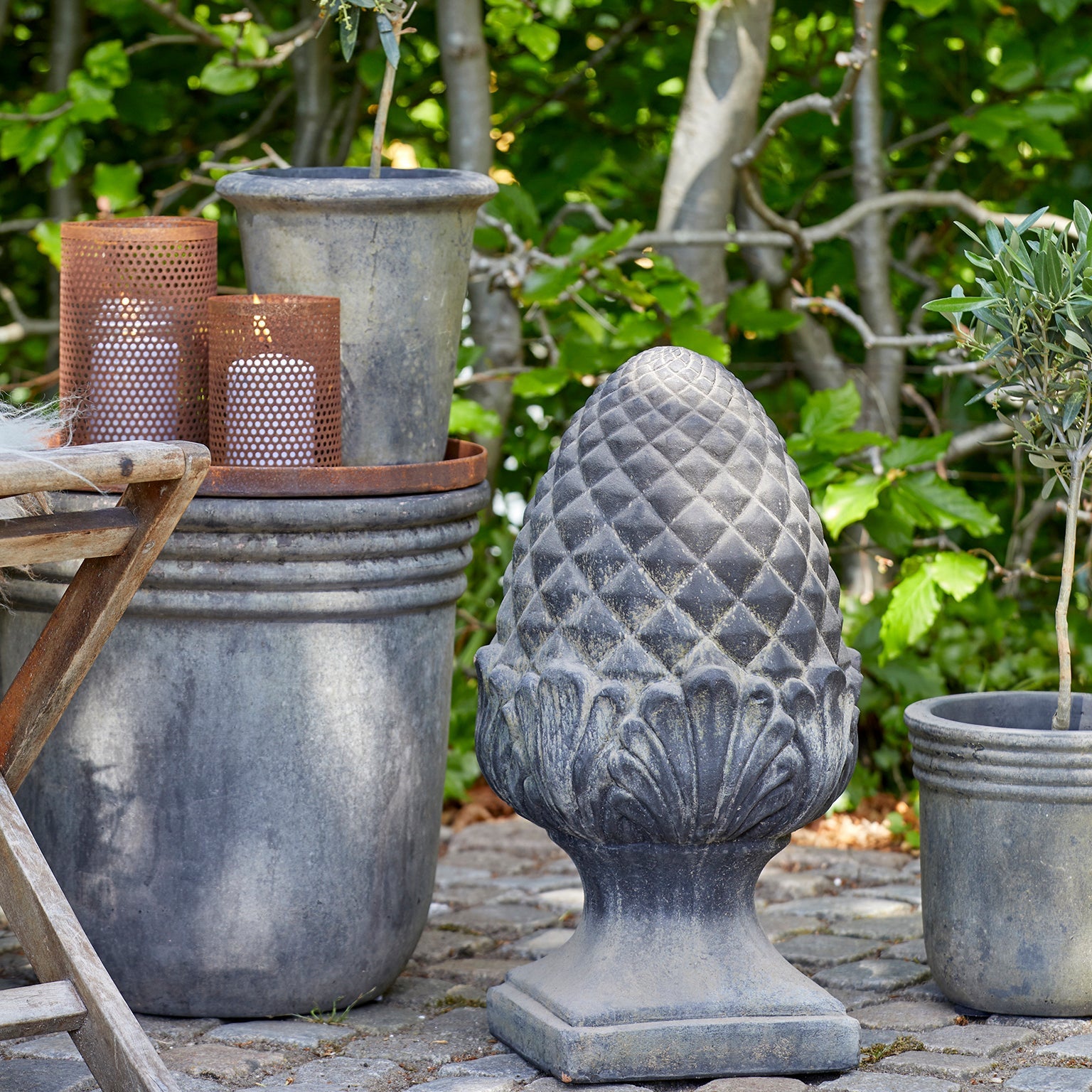 Decorative outdoor setting with potted plants and a stone finial against a natural background.