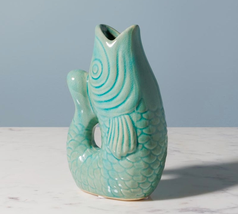 Green ceramic fish-shaped vase on a marble surface with a gray background