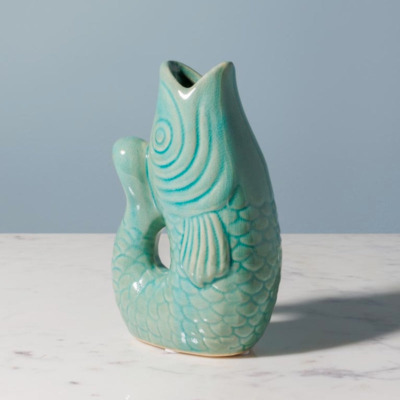 Green ceramic fish-shaped vase on a marble surface with a gray background