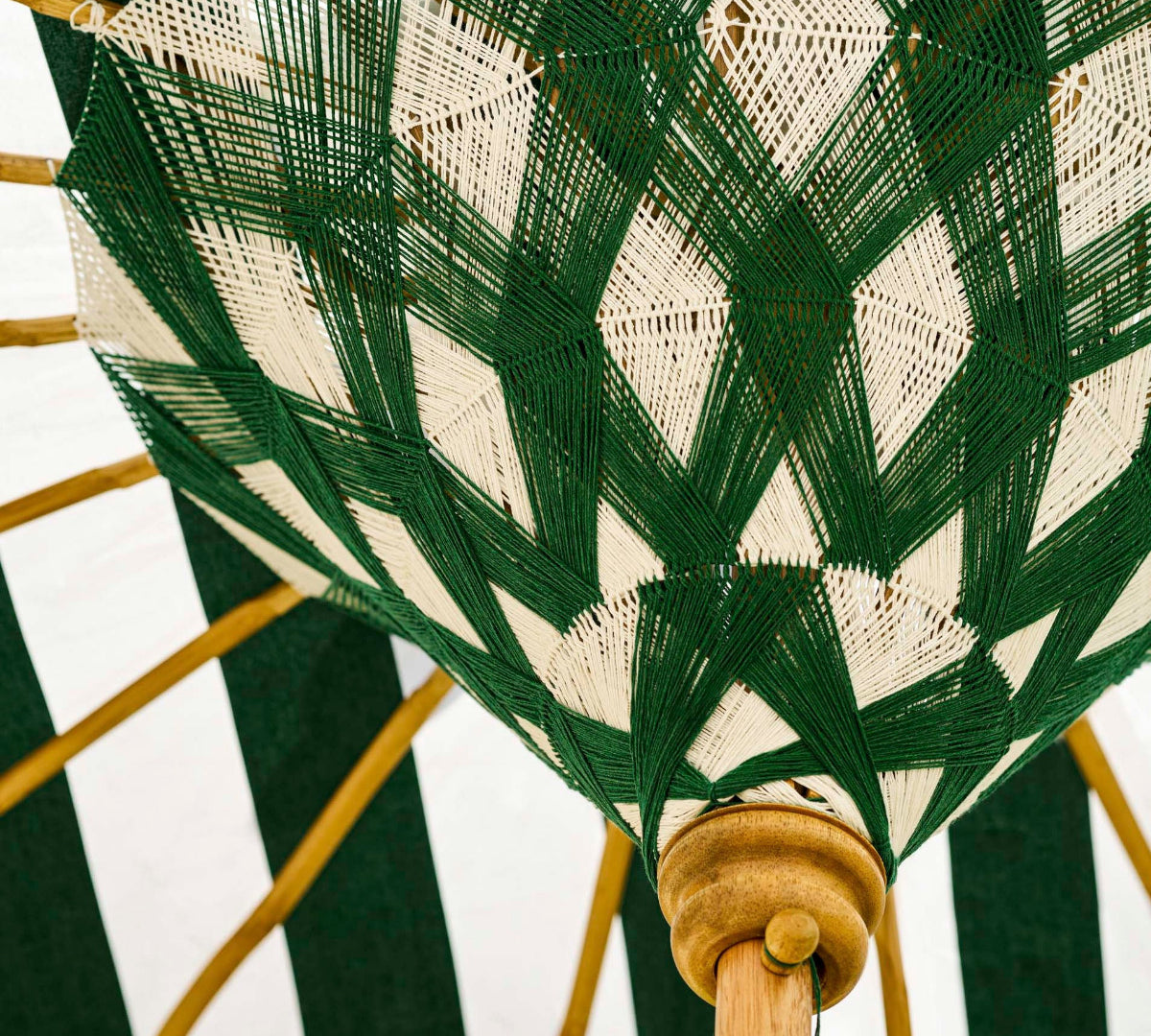 A close-up of a woven umbrella canopy with a green and off-white geometric pattern, supported by natural wood ribs.