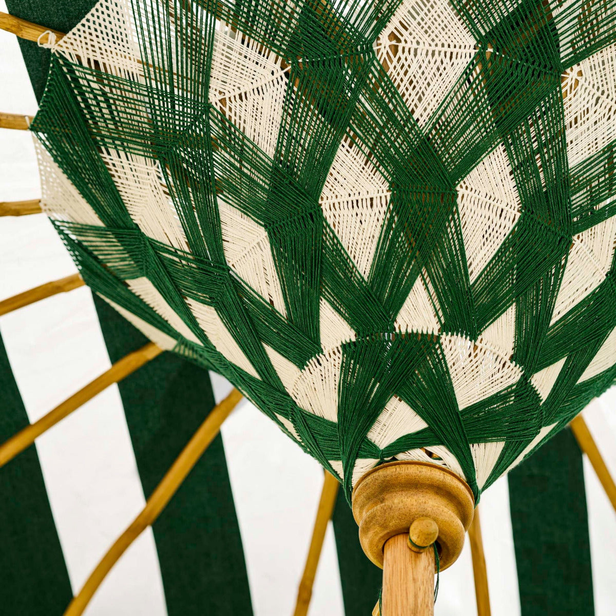 A close-up of a woven umbrella canopy with a green and off-white geometric pattern, supported by natural wood ribs.