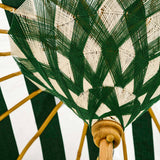 A close-up of a woven umbrella canopy with a green and off-white geometric pattern, supported by natural wood ribs.