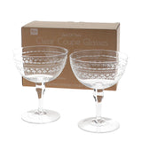 Set of two clear coupe glasses with decorative etching in front of a branded box.