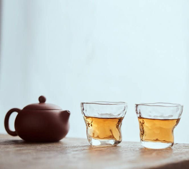 Tea set with a teapot and two glass cups on a wooden surface.