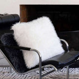 A fluffy white faux fur throw cushion and a black faux fur throw pillow resting on a black leather lounge chair in front of a fireplace.
