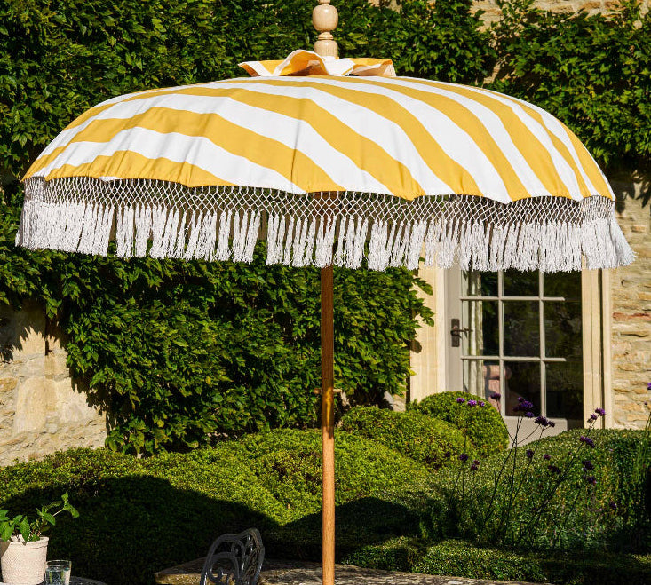 Yellow and white striped patio umbrella with fringe on a stone patio