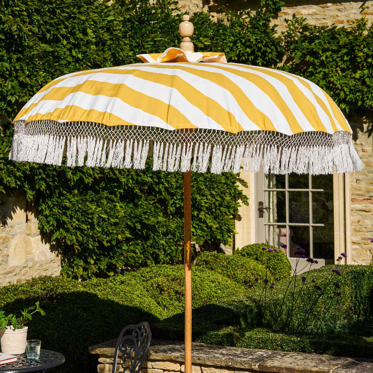 Yellow and white striped patio umbrella with fringe on a stone patio
