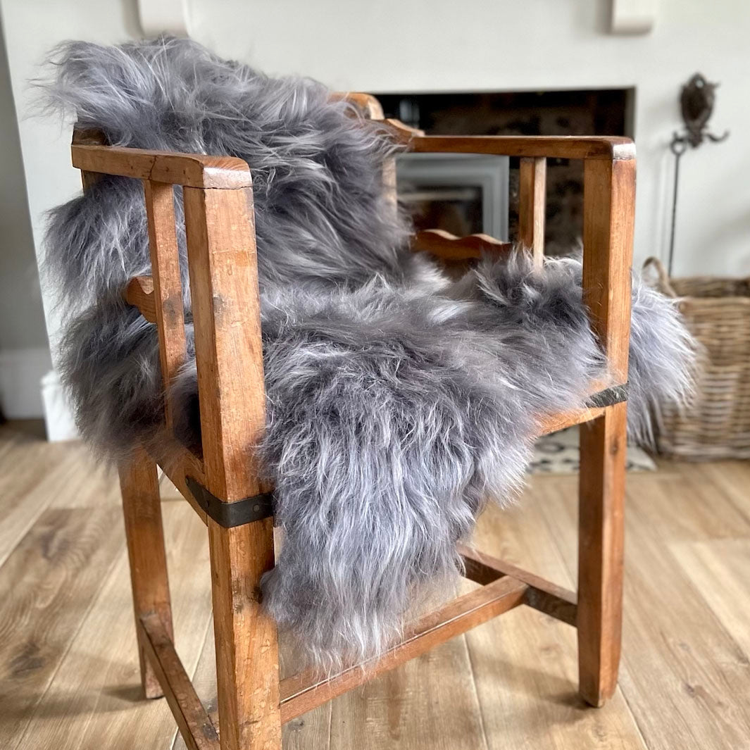 A shaggy grey Icelandic sheepskin rug draped over a wooden chair.