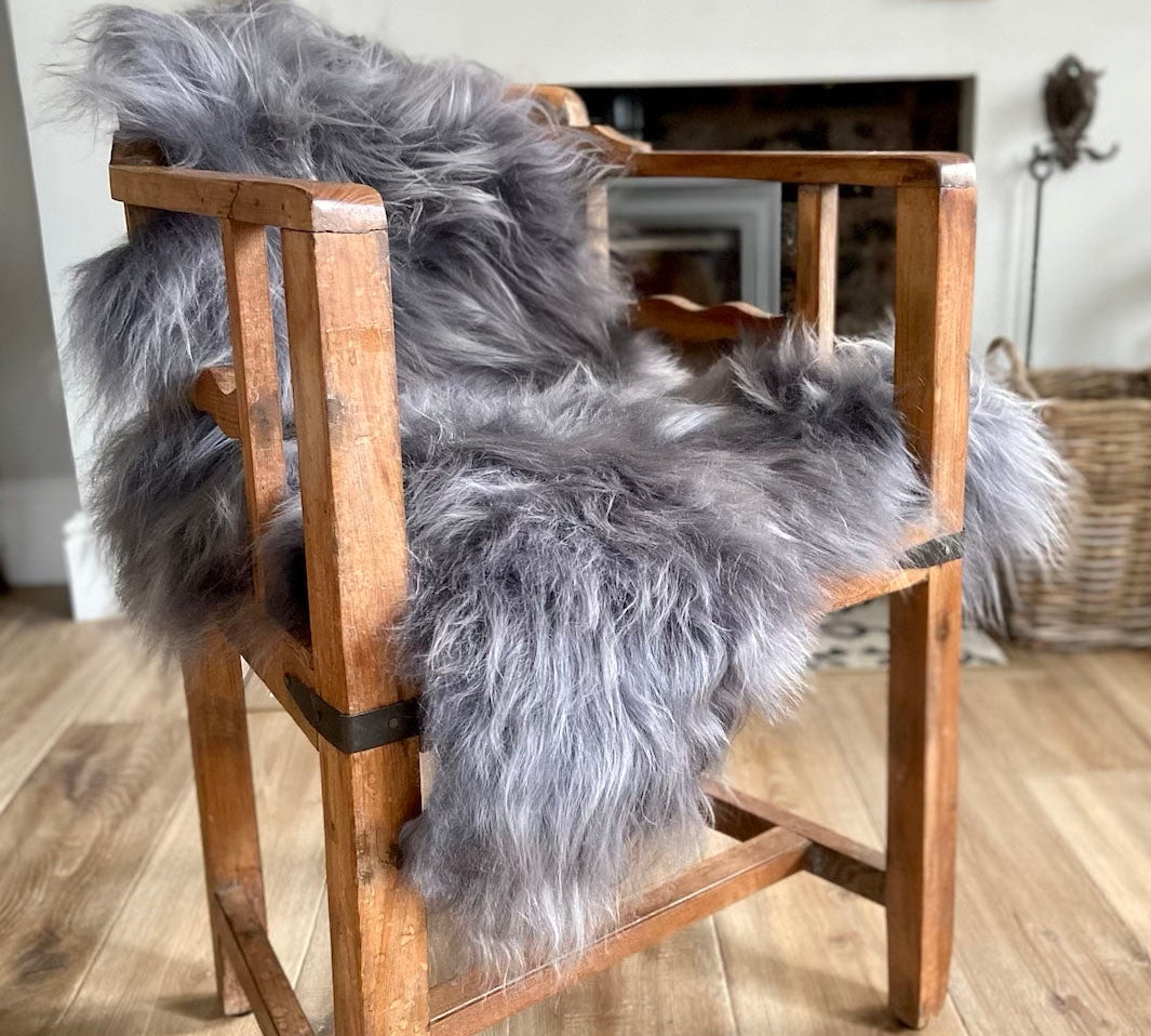 A shaggy grey Icelandic sheepskin rug draped over a wooden chair.