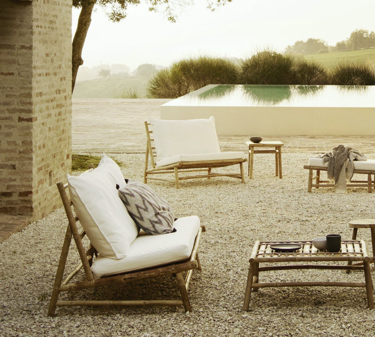 A bamboo outdoor sofa with white cushions placed in a garden setting 