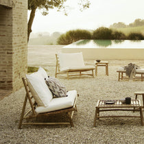 A bamboo outdoor sofa with white cushions placed in a garden setting 