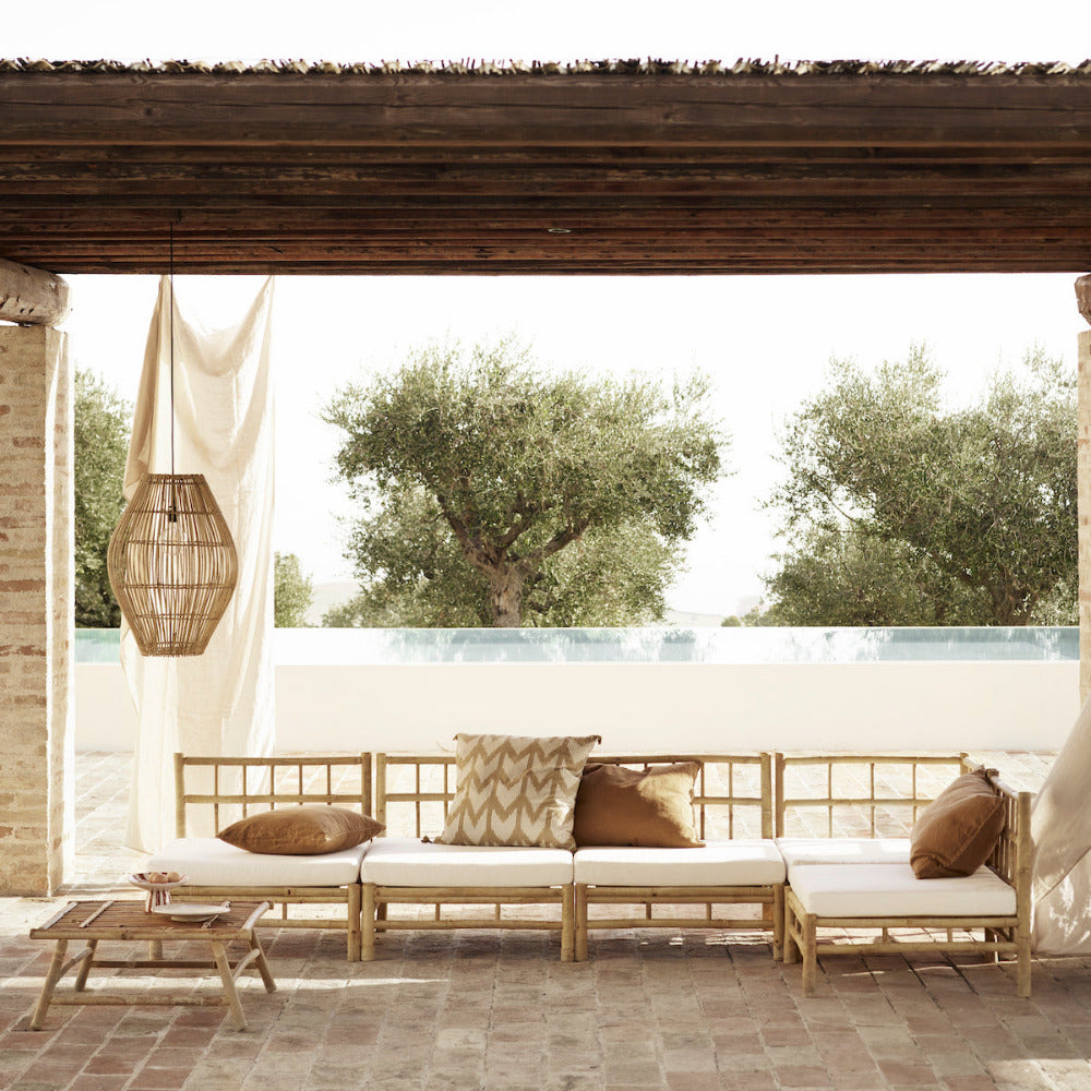 Outdoor seating area with wooden sofa and cushions, overlooking a pool and trees.
